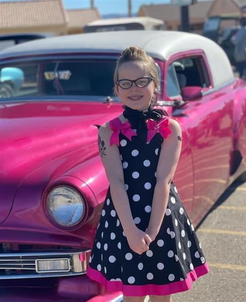 girl in a black and white poka dot dress standing in front of a pink car entry